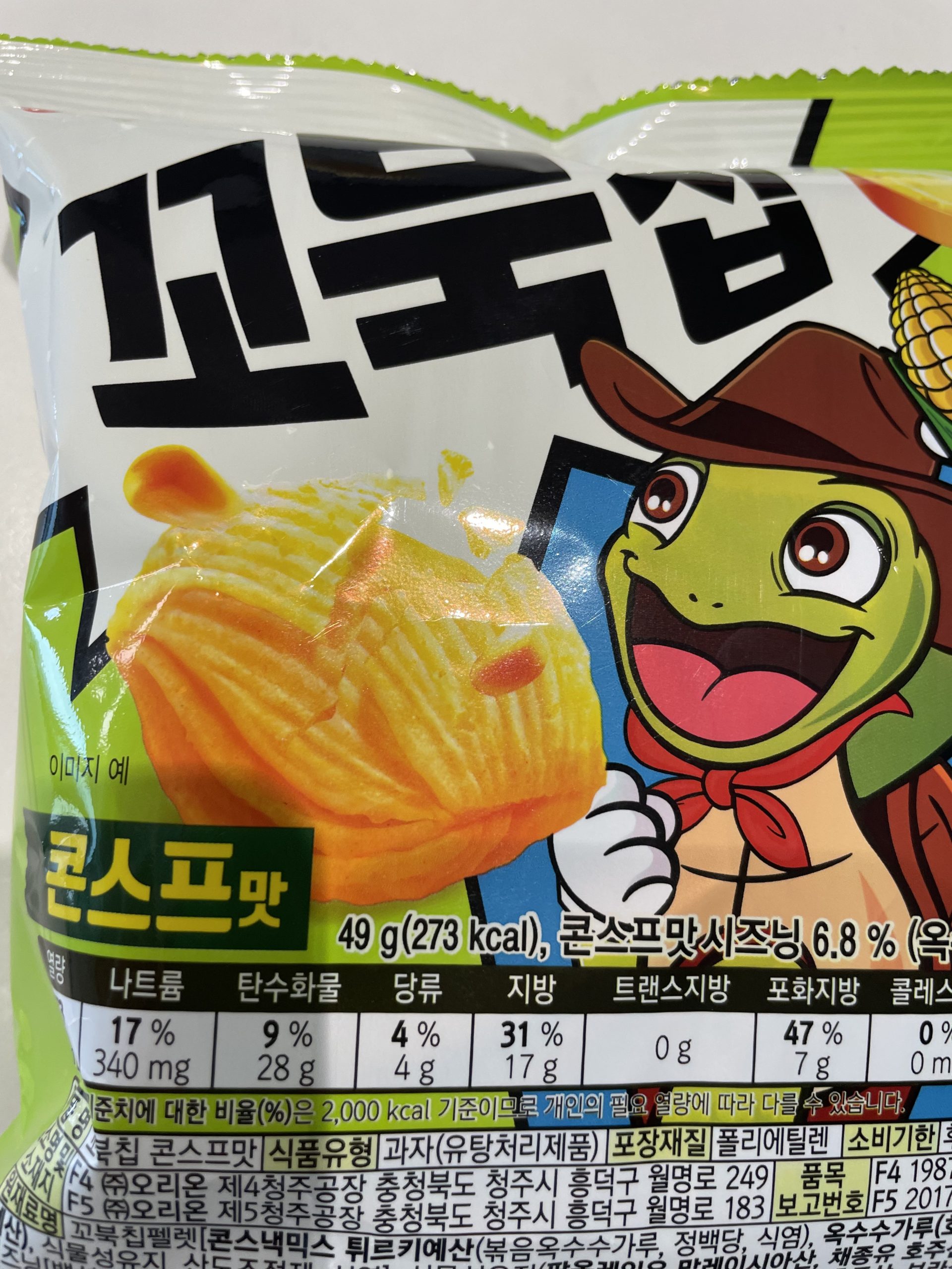 Front packaging of Orion Kkobuk Chip (Turtle Chip) Corn Soup Flavor, featuring a smiling cartoon turtle in a safari hat and an image of the multi-layered chip. The label includes prominent Korean text '꼬북칩' (Kkobuk Chip) and a clear 'Nutrition Facts' panel showing 273 kcal, 340 mg sodium, 28 g carbs, 4 g sugar, 17 g fat, 7 g saturated fat per 49 g serving.