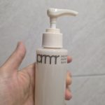 A hand holding a 100ml pump bottle of pmr Mild Facial cleanser against a light gray tiled wall, featuring a clean minimalist beige-and-white design.