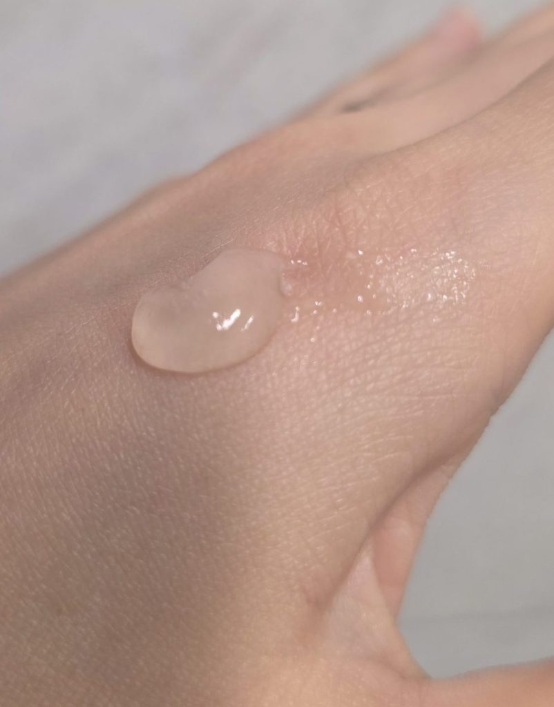 A close-up view of a drop of translucent gel cleanser texture dispensed on the back of a hand, highlighting its lightweight, moist, and clear formula.