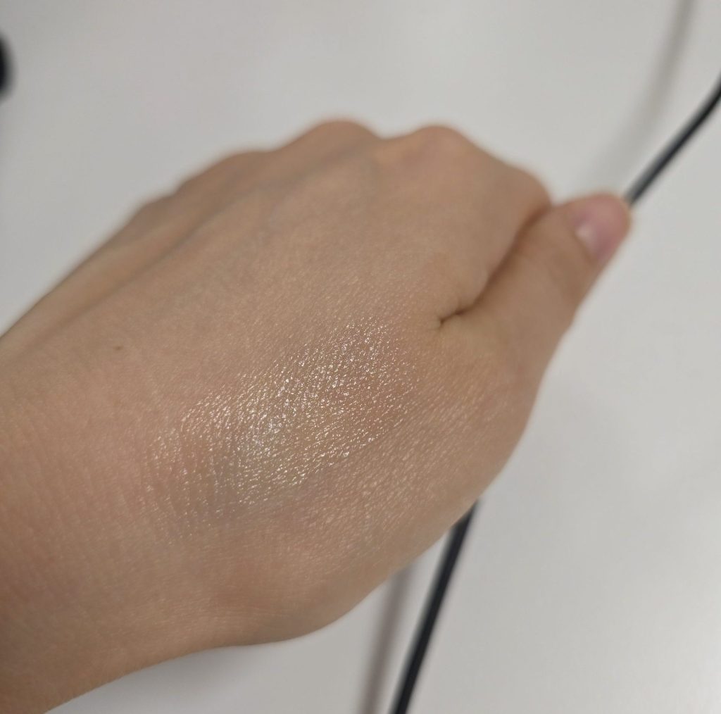 Close-up of a pearlescent shimmer swatch applied on the back of a hand, showing a detailed glistening glitter texture.