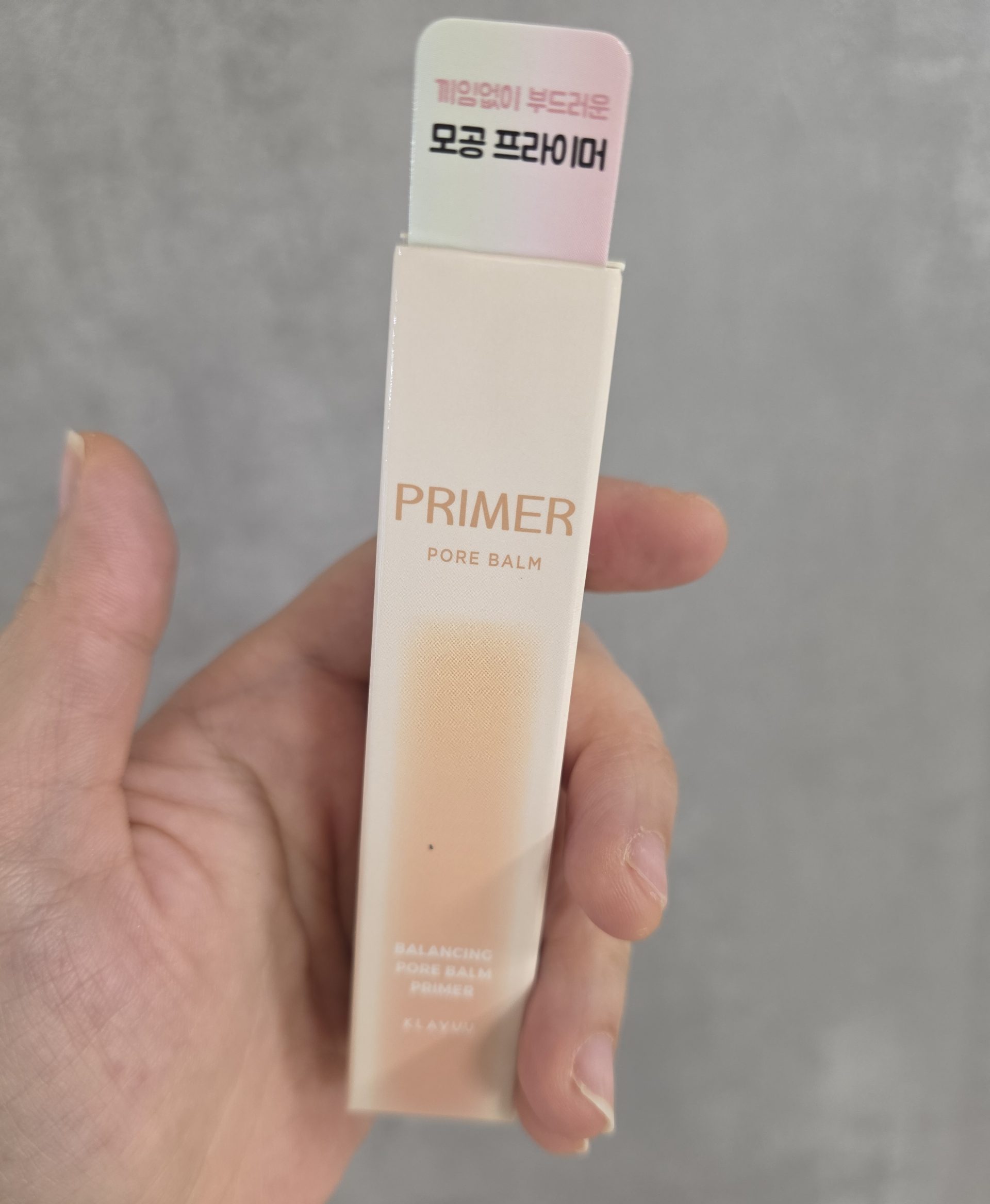 Hand holding a box of Klavuu Pore Balm Primer for smooth skin texture.