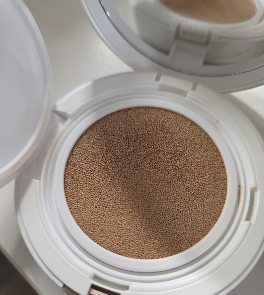 An opened cushion foundation compact showing the foundation-saturated porous sponge and inner mirror.